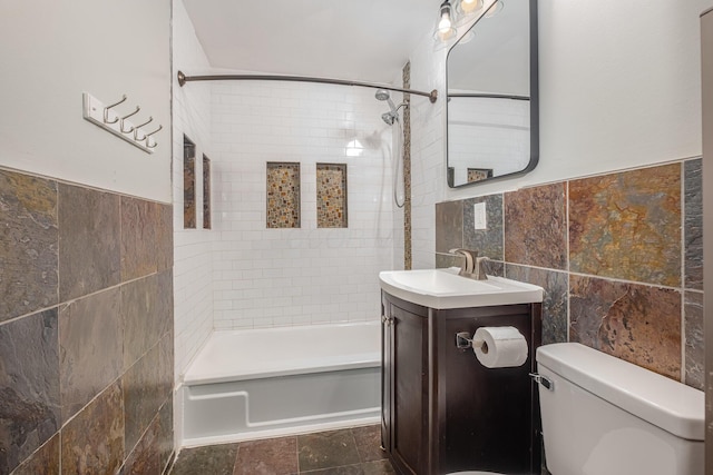 bathroom with tile walls, toilet, washtub / shower combination, vanity, and wainscoting