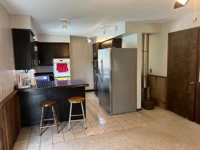 1886 Johnstown Utica Rd NE, Utica, OH 43080 - kitchen featuring stainless steel fridge, a peninsula, a wainscoted wall, dark countertops, and white double oven