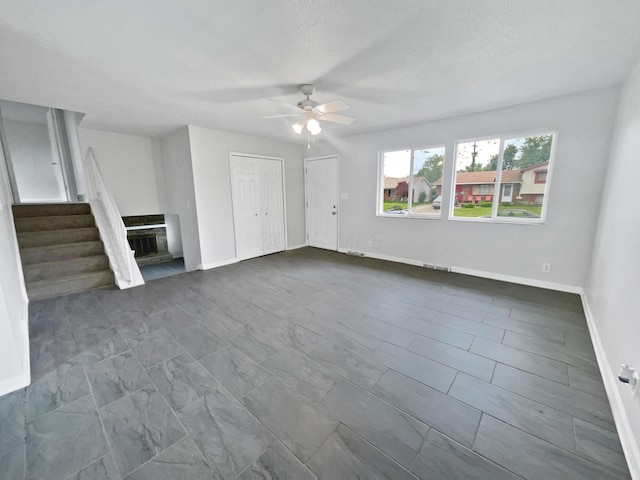 unfurnished living room featuring ceiling fan, baseboards, and stairway