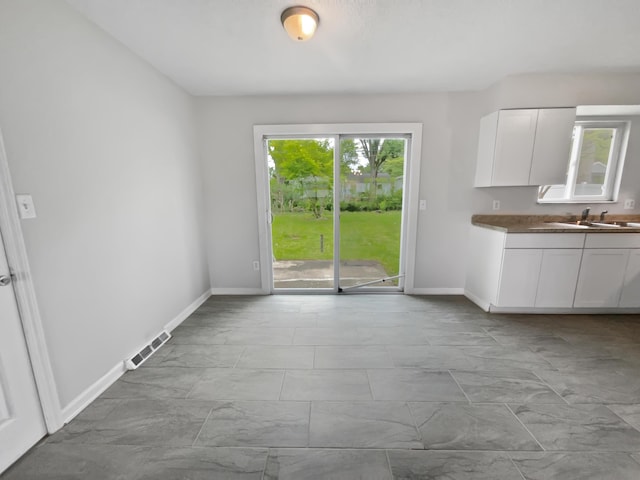 kitchen featuring a sink, light marble finish floors, white cabinets, and baseboards