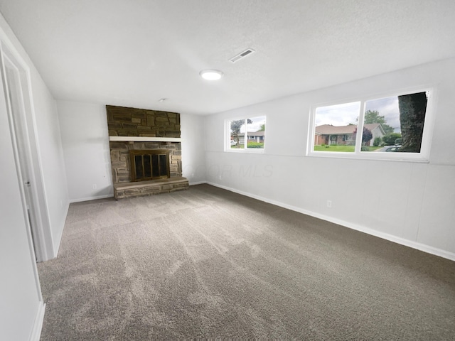 unfurnished living room featuring carpet, a stone fireplace, and baseboards