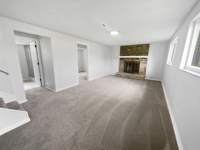 unfurnished living room with carpet flooring, a stone fireplace, stairs, and baseboards