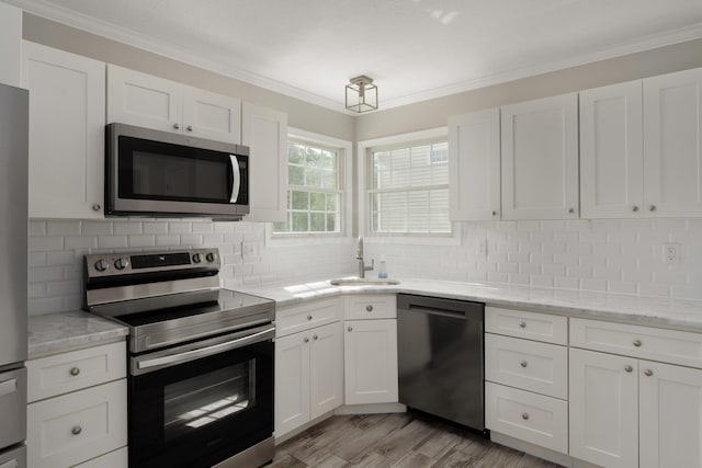 4526 Hoffman Farms Dr, Hilliard, OH 43026 - kitchen with appliances with stainless steel finishes, a sink, white cabinets, crown molding, and light wood-style flooring
