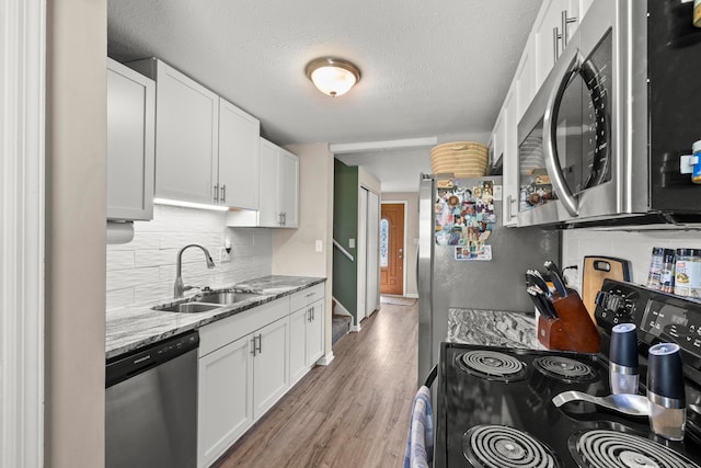 2267 Anndel Ct, Grove City, OH 43123 - kitchen with stainless steel appliances, a sink, decorative backsplash, white cabinets, and light wood-type flooring