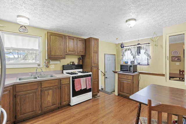 kitchen featuring white range with gas stovetop, a sink, stainless steel microwave, light wood-type flooring, and brown cabinetry