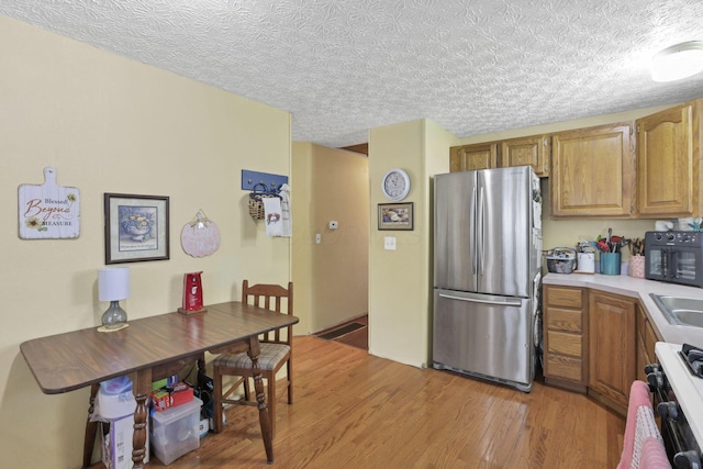 kitchen with freestanding refrigerator, light wood-type flooring, light countertops, brown cabinets, and a textured ceiling