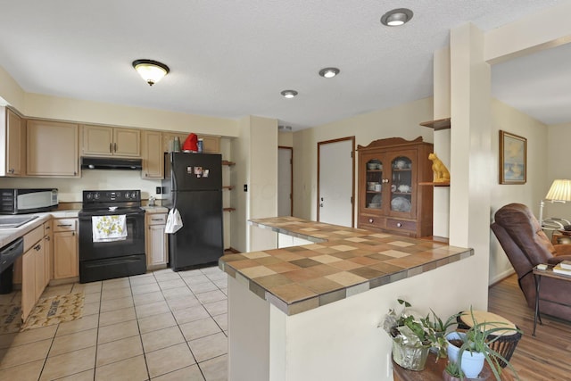 1703 Ringfield Dr, Galloway, OH 43119 - kitchen featuring black appliances, under cabinet range hood, a peninsula, tile counters, and light brown cabinetry