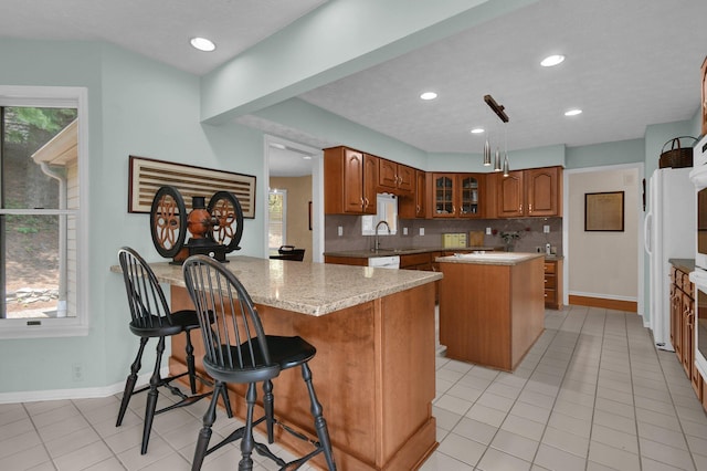 71 Donald Ross Dr, Granville, OH 43023 - kitchen featuring a center island, a peninsula, brown cabinets, light tile patterned floors, and glass insert cabinets