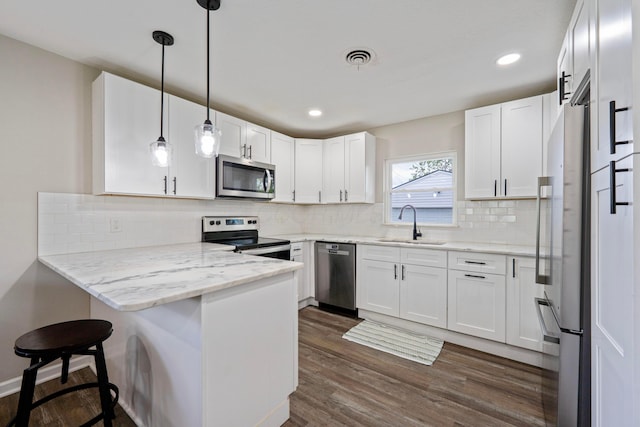 kitchen featuring appliances with stainless steel finishes, a peninsula, a sink, white cabinetry, and dark wood finished floors