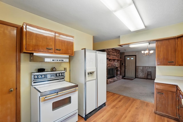 kitchen featuring white appliances, under cabinet range hood, brown cabinetry, a chandelier, and light wood-style floors