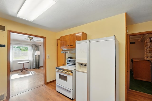 kitchen featuring white appliances, light wood-type flooring, under cabinet range hood, and brown cabinetry
