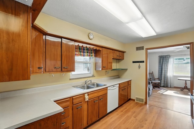 kitchen featuring a sink, white dishwasher, light countertops, light wood-style flooring, and brown cabinets