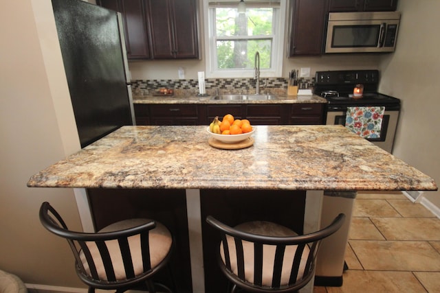 kitchen with stainless steel appliances, a sink, a kitchen breakfast bar, and dark brown cabinetry