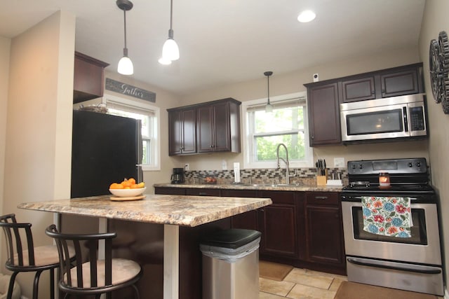 kitchen featuring appliances with stainless steel finishes, a sink, dark brown cabinetry, a breakfast bar, and light stone countertops