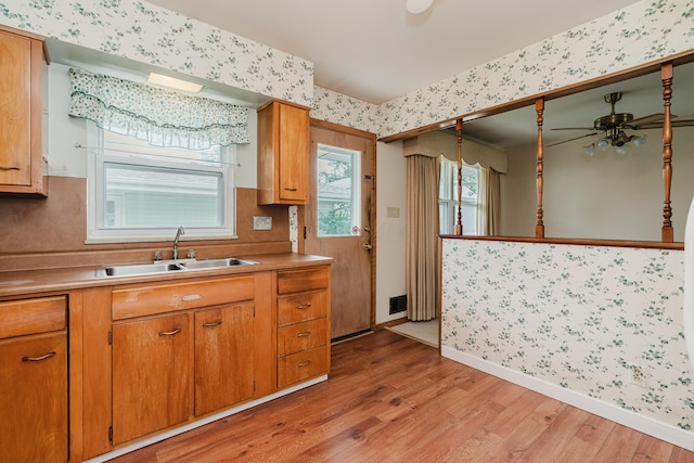 kitchen with wallpapered walls, a sink, light wood-type flooring, ceiling fan, and baseboards