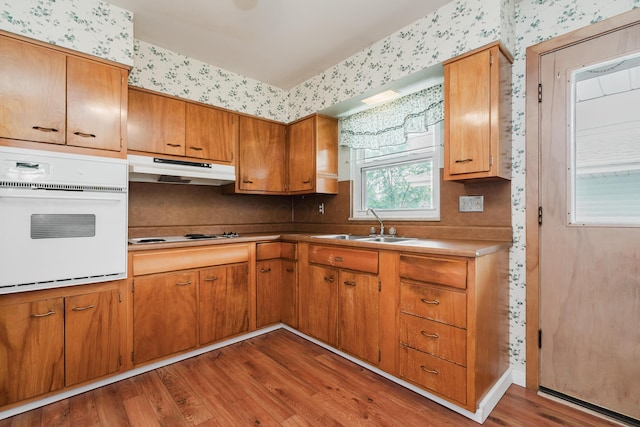 kitchen featuring wallpapered walls, under cabinet range hood, white appliances, wood finished floors, and brown cabinets