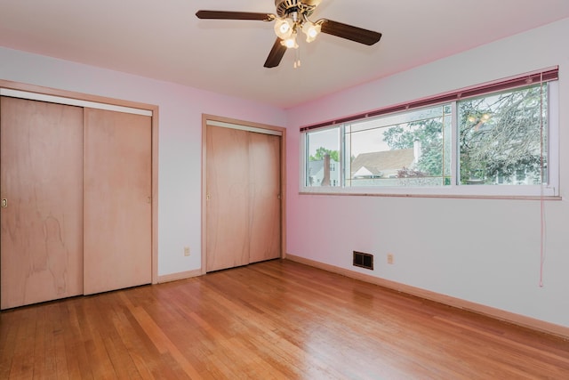 unfurnished bedroom with two closets, light wood-style floors, baseboards, and ceiling fan
