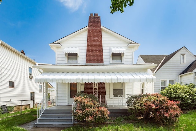 view of front of house with covered porch, a chimney, and fence