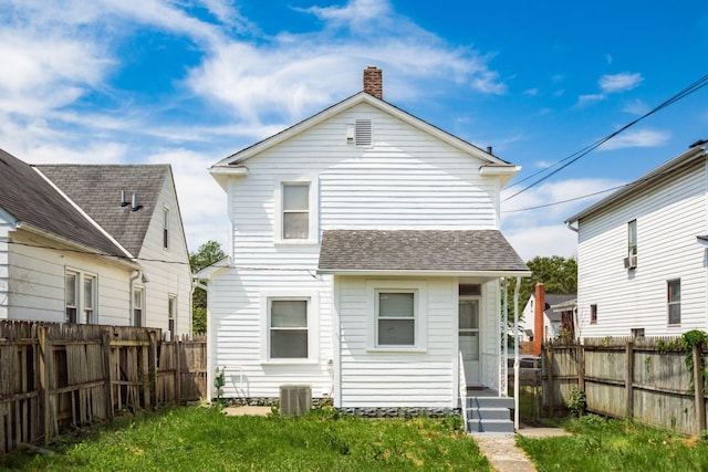 back of property featuring a chimney, a fenced backyard, a shingled roof, and central AC