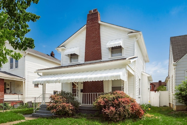 view of front of property featuring a chimney, fence, brick siding, and a porch