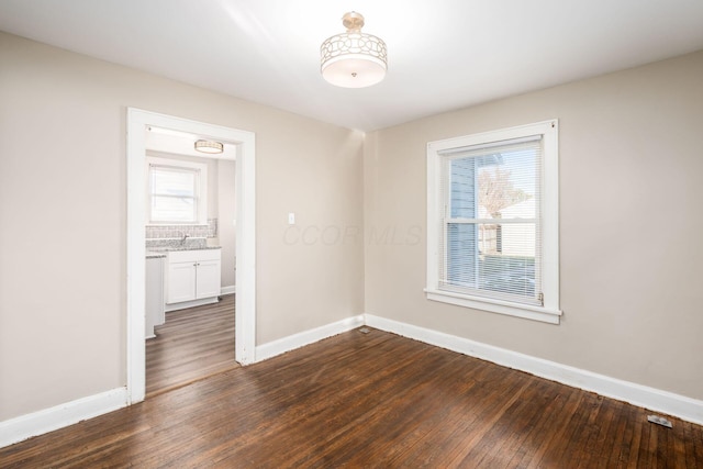 empty room featuring dark wood finished floors, baseboards, and a sink
