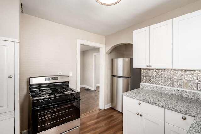 kitchen with stainless steel appliances, white cabinetry, dark wood-style flooring, light stone counters, and baseboards