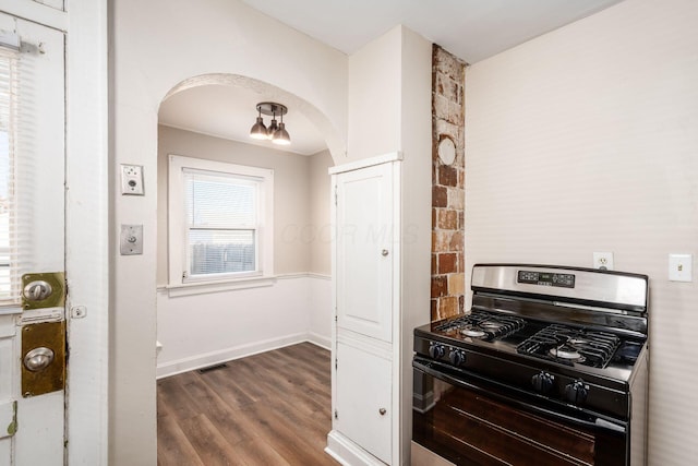 kitchen featuring gas range oven, arched walkways, dark wood-style flooring, and baseboards