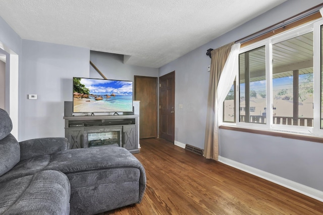 living area with dark wood-style flooring, baseboards, a textured ceiling, and a glass covered fireplace
