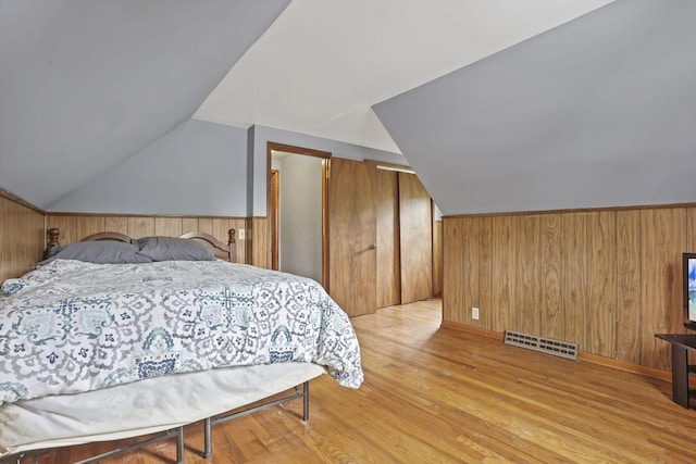 bedroom with vaulted ceiling, wooden walls, and light wood-style floors
