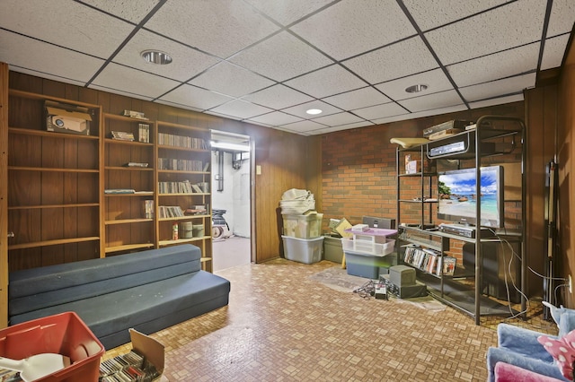 living area featuring a drop ceiling and wood walls