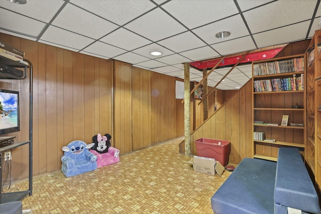 playroom with tile patterned floors, a paneled ceiling, and wood walls