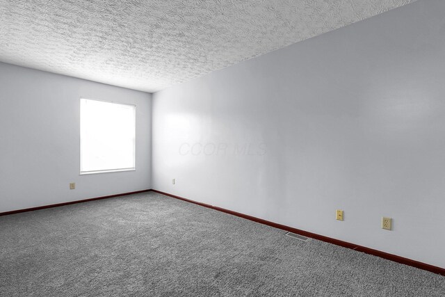 carpeted spare room featuring a textured ceiling and baseboards