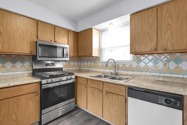 kitchen featuring stainless steel appliances, a sink, light countertops, decorative backsplash, and wood finished floors