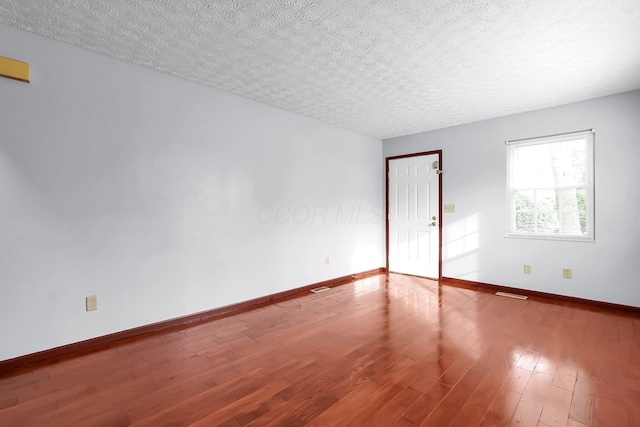 unfurnished room with baseboards, wood finished floors, and a textured ceiling