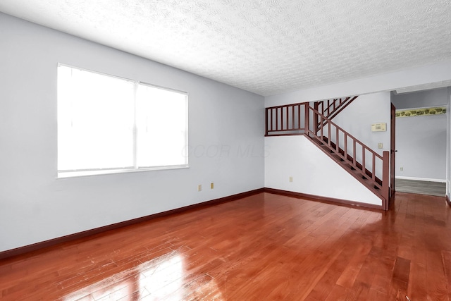 spare room featuring stairway, baseboards, hardwood / wood-style floors, and a textured ceiling