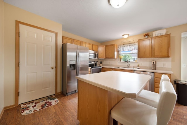 kitchen with appliances with stainless steel finishes, a sink, light countertops, a center island, and a kitchen breakfast bar