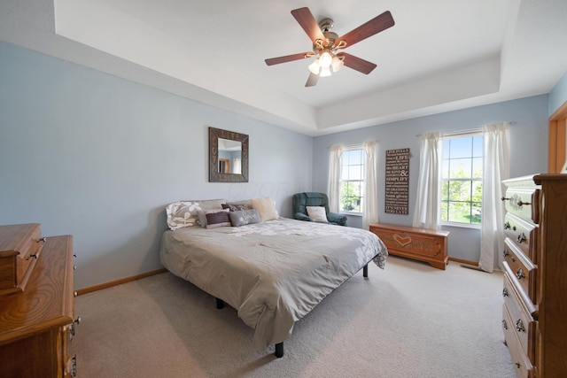 bedroom featuring a tray ceiling, baseboards, light colored carpet, and a ceiling fan