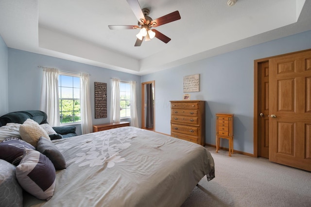 bedroom featuring a raised ceiling, light carpet, baseboards, and ceiling fan