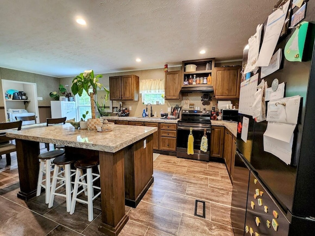 kitchen with stainless steel range with electric stovetop, a center island, a kitchen breakfast bar, light countertops, and brown cabinetry