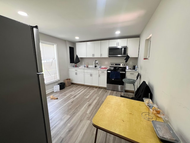 2624 Osceola Ave, Columbus, OH 43211 - kitchen featuring stainless steel appliances, white cabinets, a sink, light wood finished floors, and light countertops