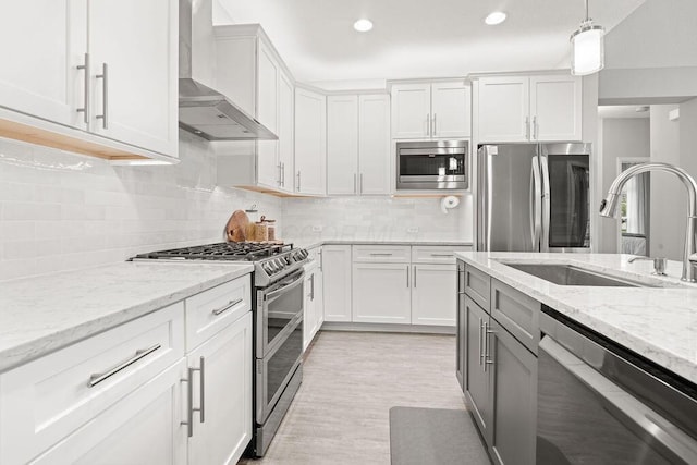 5165 Hamptonshire Dr, Dublin, OH 43016 - kitchen featuring appliances with stainless steel finishes, wall chimney range hood, a sink, white cabinets, and pendant lighting