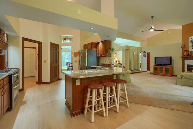 3695 Britton Ave, Columbus, OH 43204 - kitchen featuring stainless steel appliances, a breakfast bar area, light wood-type flooring, brown cabinetry, and high vaulted ceiling