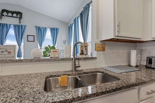 4196 Holstein Dr, Obetz, OH 43207 - kitchen with a sink, vaulted ceiling, white cabinetry, dark stone countertops, and backsplash