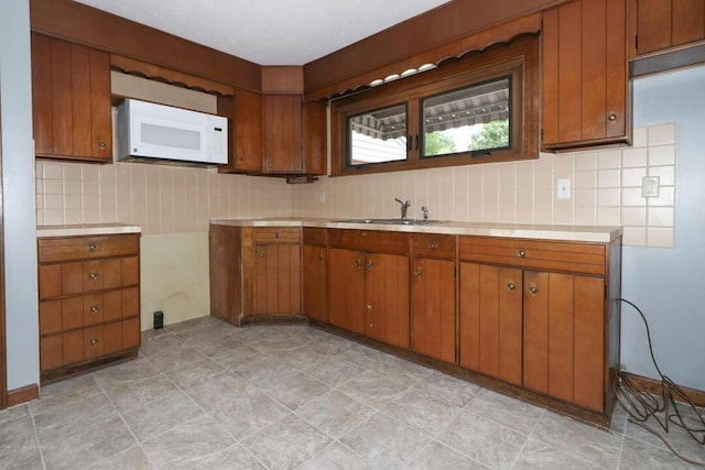 1266 Hanley Rd W, Mansfield, OH 44903 - kitchen featuring white microwave, a sink, light countertops, brown cabinetry, and tasteful backsplash