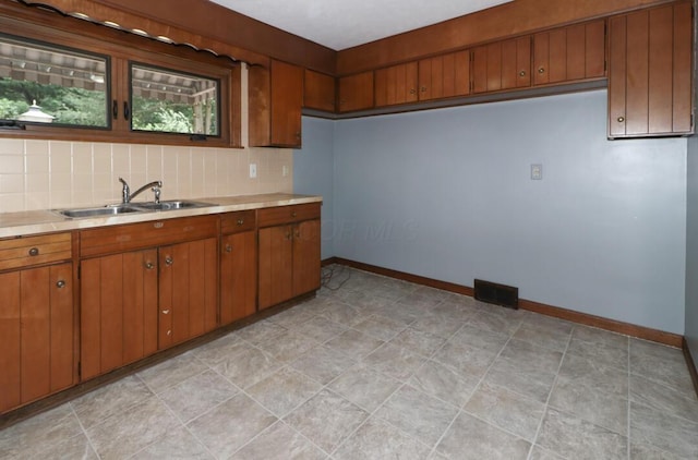 1266 Hanley Rd W, Mansfield, OH 44903 - kitchen featuring a sink, light countertops, brown cabinets, tasteful backsplash, and baseboards