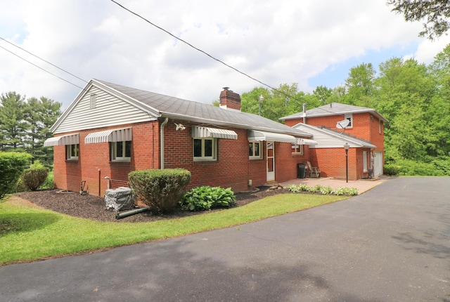 1266 Hanley Rd W, Mansfield, OH 44903 - view of side of home featuring brick siding, a chimney, asphalt driveway, and a lawn