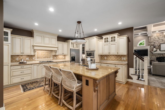 712 Riverbend Ave, Powell, OH 43065 - kitchen featuring appliances with stainless steel finishes, light wood finished floors, light stone counters, an island with sink, and decorative backsplash