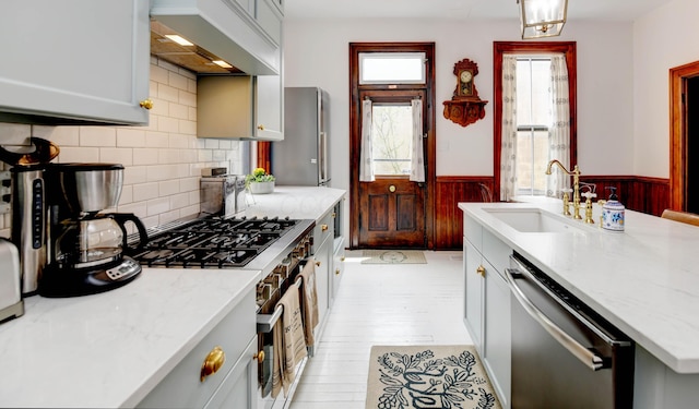 758 S Front St, Columbus, OH 43206 - kitchen with dishwasher, a sink, a wainscoted wall, wall chimney range hood, and stove