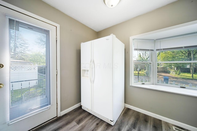 kitchen featuring white fridge with ice dispenser, dark wood-style flooring, and baseboards