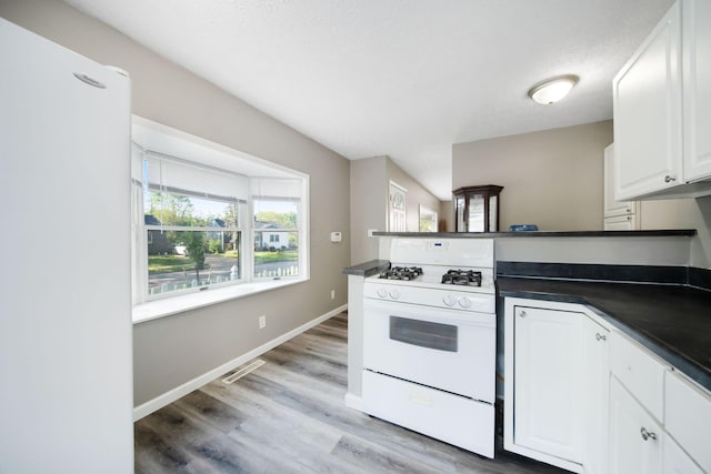 kitchen with white gas range oven, a peninsula, dark countertops, and white cabinetry